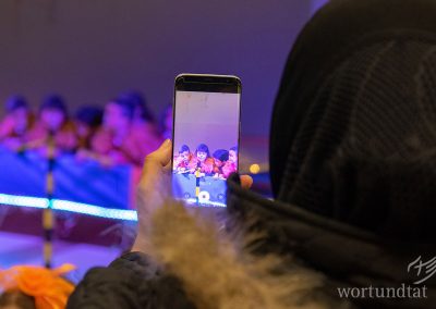 Woman with headscarf films with smartphone children made up and dressed up like lions.