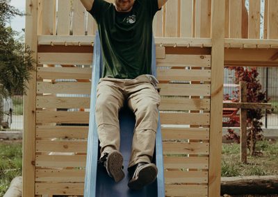 Adults being kids sliding down the slide with raised hands.