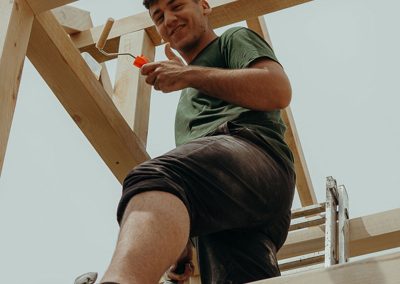 Mann streicht Holzbalken eines Klettergerüsts