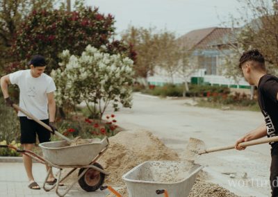 Two men shovel sand into wheelbarrows