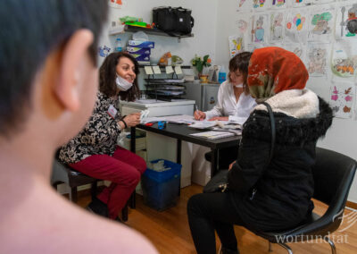 Drei Frauen an Tisch - zwei sprechen miteinander - die dritte schreibt etwas - Flüchtlinge in Griechenland