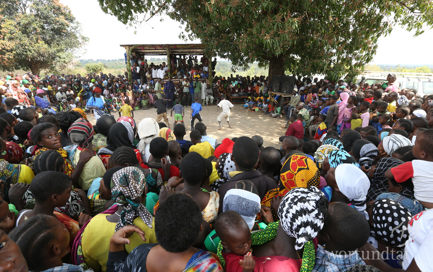 Bei der Eröffnung eines Hoffnungszentrums versammelt sich das ganze Dorf, um mitzufeiern. Menschenmenge - in der Mitte freier Platz auf dem Kinder einen Tanz vorführen