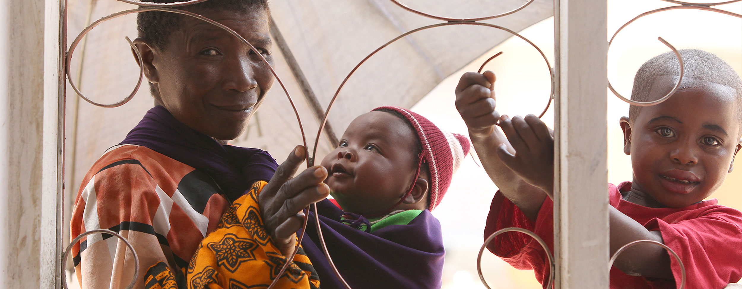 Frau mit Baby und Kind schauen durch vergittertes Fenster Frau mit Baby und Kind schauen durch vergittertes Fenster
