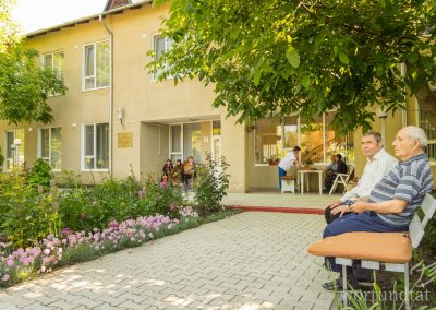 Two men on a bench in front of a building - flowers blooming in garden