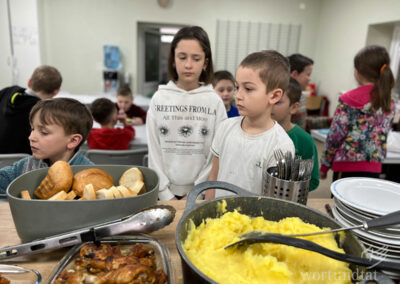 3 Kinder vor einem Tisch mit Kartoffelpüree, Hähnchenbollen und Brot