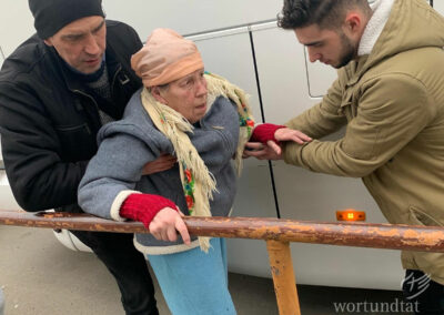 Zwei Männer stützen eine ältere Frau