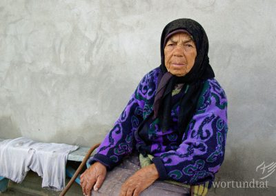 Old woman on bench in front of her house, simply dressed
