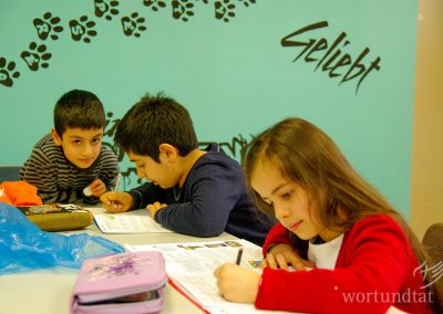 three children at the table writing in workbooks - helping children in Germany