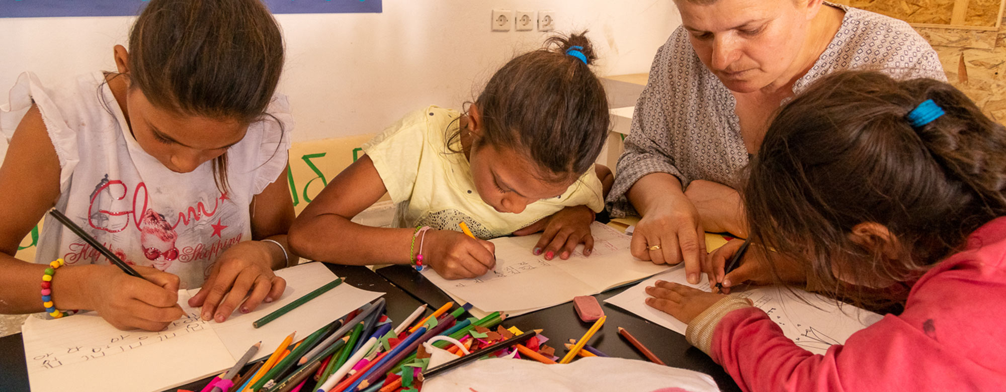 Drei Mädchen malen und basteln an einem Tisch zusammen mit einer Betreuuerin Gruppenbild von Kindern und ihren erwachsenen Betreuern