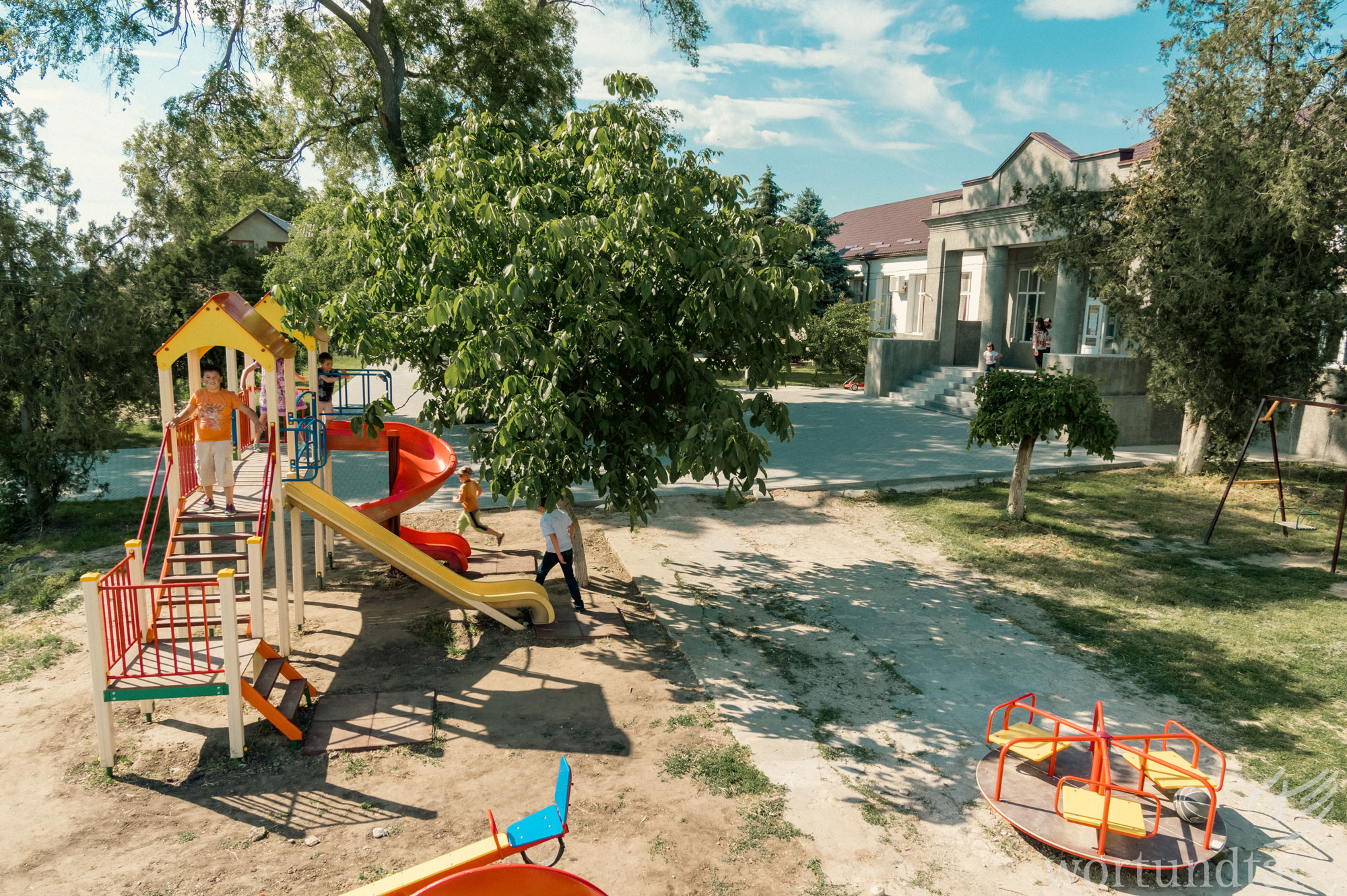 In der Kindertagesstätte in Vulkanesti haben die Kinder großartige Möglichkeiten, zu spielen, Gemeinschaft zu erfahren, Hiilfe bein den Hausarbeiten zu bekommen oder ein gesundes Mittagessen zu erhalten. Gebäude mit großzügigem Garten, Spielgeräten und Bäumen bei Sonnenschein.