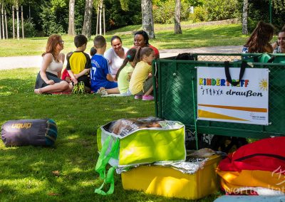 Children in Dortmund sitting on a meadow - a handcart with the inscription Kids meeting outside is standing by - helping children in Germany