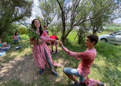 Two teenagers playing theatre - he kneels - she stands with a bouquet of flowers