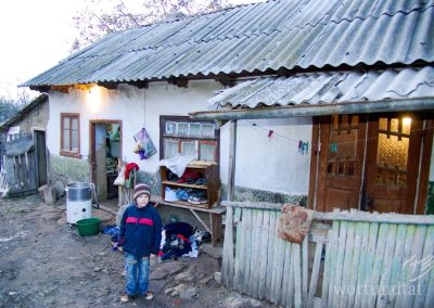 House in disrepair, boy looking sad in front of it