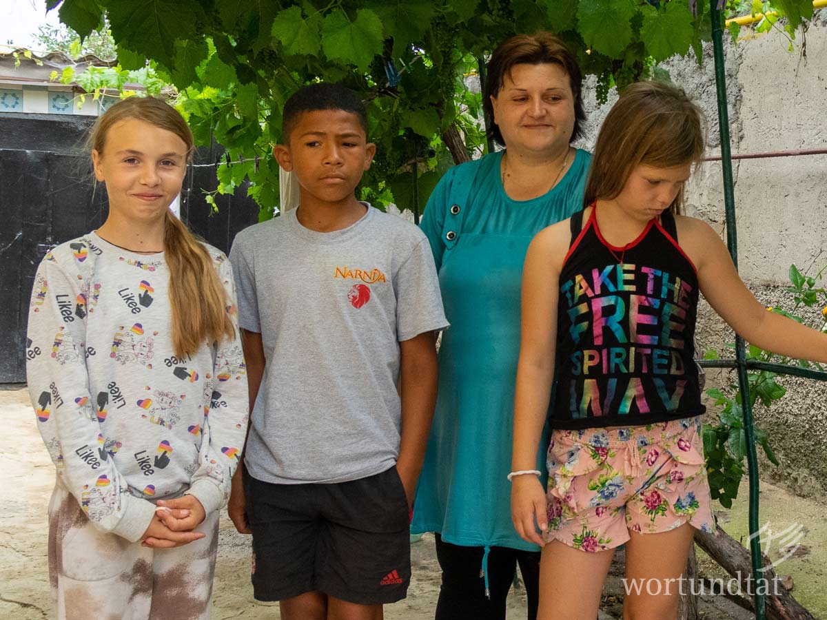 Sjuscha (12 Jahre), Oliver (11 Jahre), Valeria (11 Jahre) leben zusammen mit der Mutter der beiden Mädchen, einer Oma und einer weiteren Verwandten in einem Appartement mit etwa 30 Quadratmetern. Die Unterkunft ist in drei Zimmer und eine Küche aufgeteilt. Ein Holzofen heizt die Wohnung. Im Winter 2021/22 reichte das Holz nur zum einmaligen Heizen pro Tag. So kühlte das Haus bis zum Abend auf 10 Grad ab, bevor wieder angefeuert wurde. Drei Kinder und Frau haben sich für Foto aufgestellt