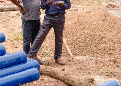 Two men looking at a plan - blue plastic tubes and a heap of gravel on the ground